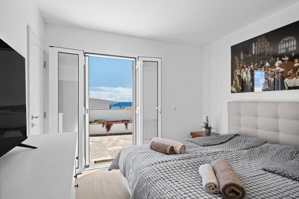 A bedroom with a bed, a TV, a painting, and a balcony with a view.