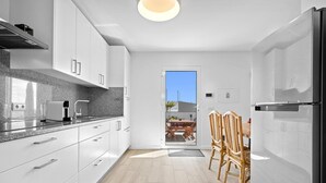A modern kitchen with white cabinets, a built-in oven, and a dining area with a table and chairs. - Holiday Home 'Casa Do Cabeco' with Sea View and Wi-Fi (Cabeco de Ponta)