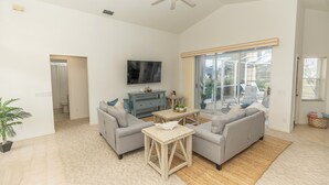A spacious living room with two grey sofas, a wooden coffee table, and a TV mounted on the wall. There is a sliding glass door leading to a balcony with a view of the outside. - Rotonda Coastal 3 bed 2.5 bath stunning pool home next to golf course! (Rotonda West)