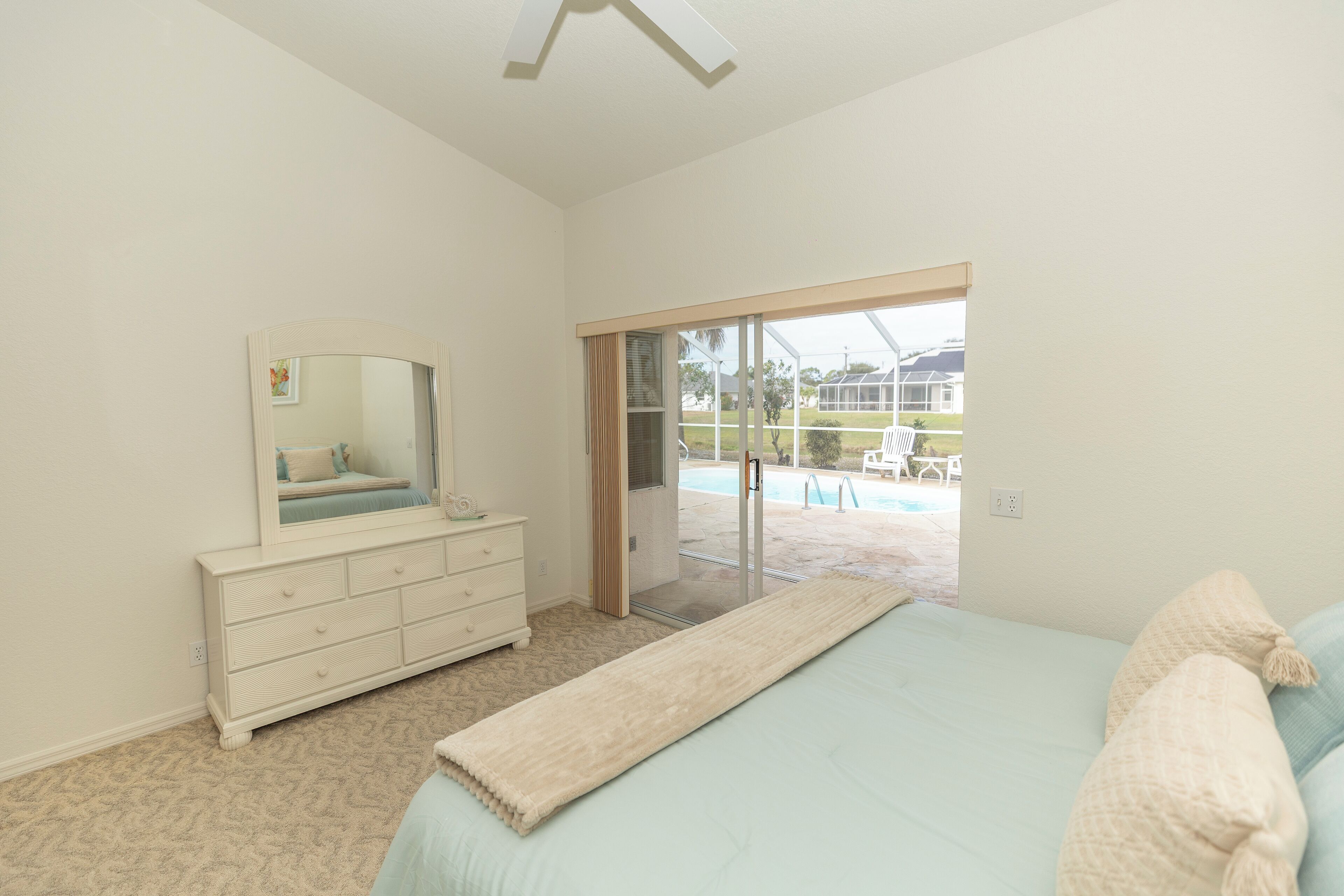Een slaapkamer met een bed, een dressoir en uitzicht op een zwembad en terras.
