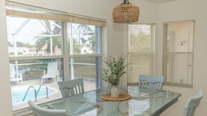 A dining area with a glass table, white chairs, a woven pendant light, and a view of a swimming pool. - Rotonda Coastal 3 bed 2.5 bath stunning pool home next to golf course! (Rotonda West)