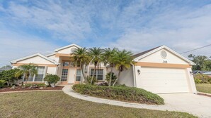 A two-story house with a garage, palm trees, and a well-maintained lawn. - Rotonda Coastal 3 bed 2.5 bath stunning pool home next to golf course! (Rotonda West)