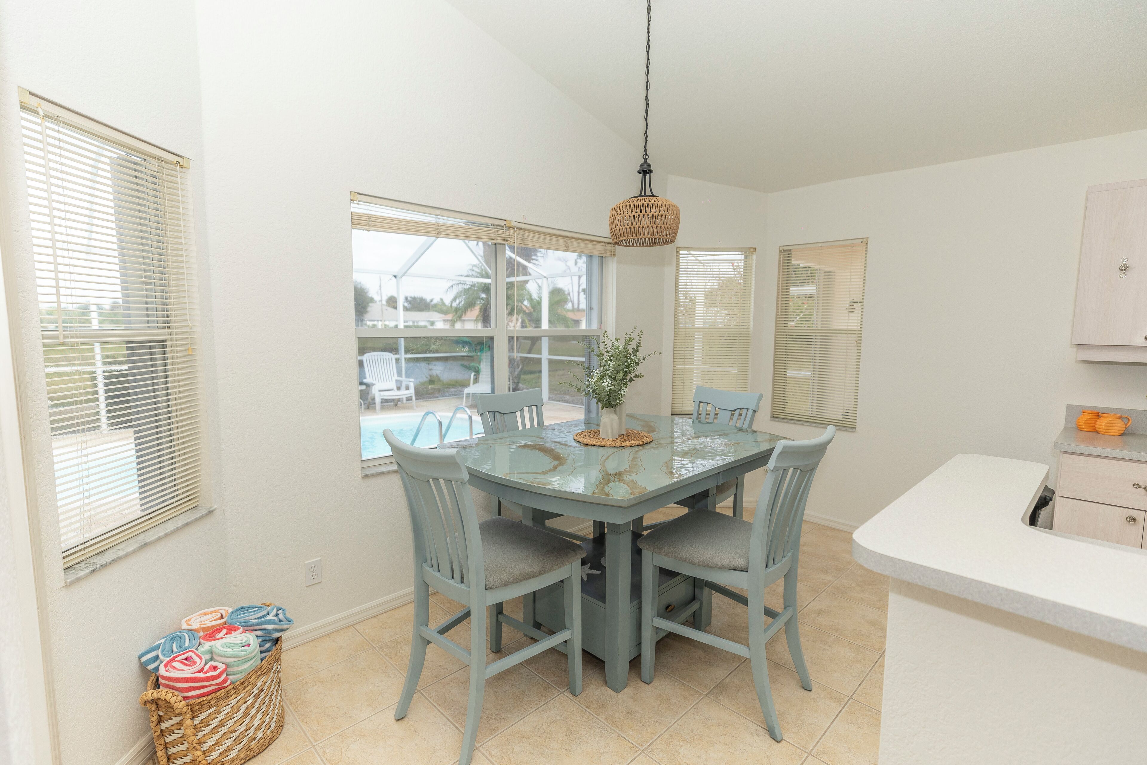 A dining area with a glass table, four chairs, and a hanging light fixture.