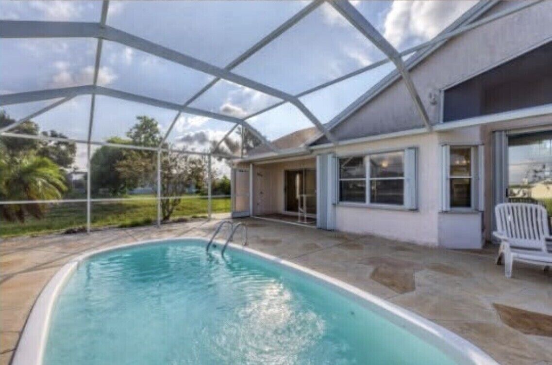 Una piscina exterior techada con techo transparente, un patio de piedra y una silla blanca.