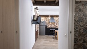 A narrow hallway leading to a kitchen with a stone backsplash, a modern refrigerator, and a TV mounted on the wall. - Casa Pietra Bianca | Cornino Bay | Modern comfort | Private pool | Sicily (Castellammare del Golfo)