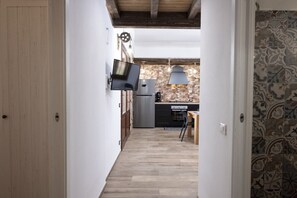 Un pasillo estrecho que da a una cocina con salpicadero de piedra, un refrigerador moderno y un televisor montado en la pared.
