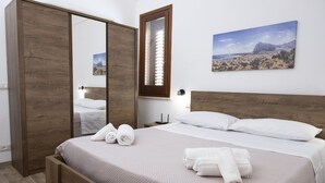 A bedroom with a wooden bed, a large mirror, a painting of a desert landscape, and neatly folded towels. - Casa Pietra Bianca | Cornino Bay | Modern comfort | Private pool | Sicily (Castellammare del Golfo)