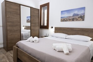 A bedroom with a wooden bed, a large mirror, a painting of a desert landscape, and neatly folded towels. - Casa Pietra Bianca | Cornino Bay | Modern comfort | Private pool | Sicily (Castellammare del Golfo)