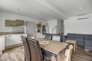 Une cuisine moderne avec des meubles blancs, une table à manger avec des chaises, un canapé gris et un escalier menant à un autre niveau.