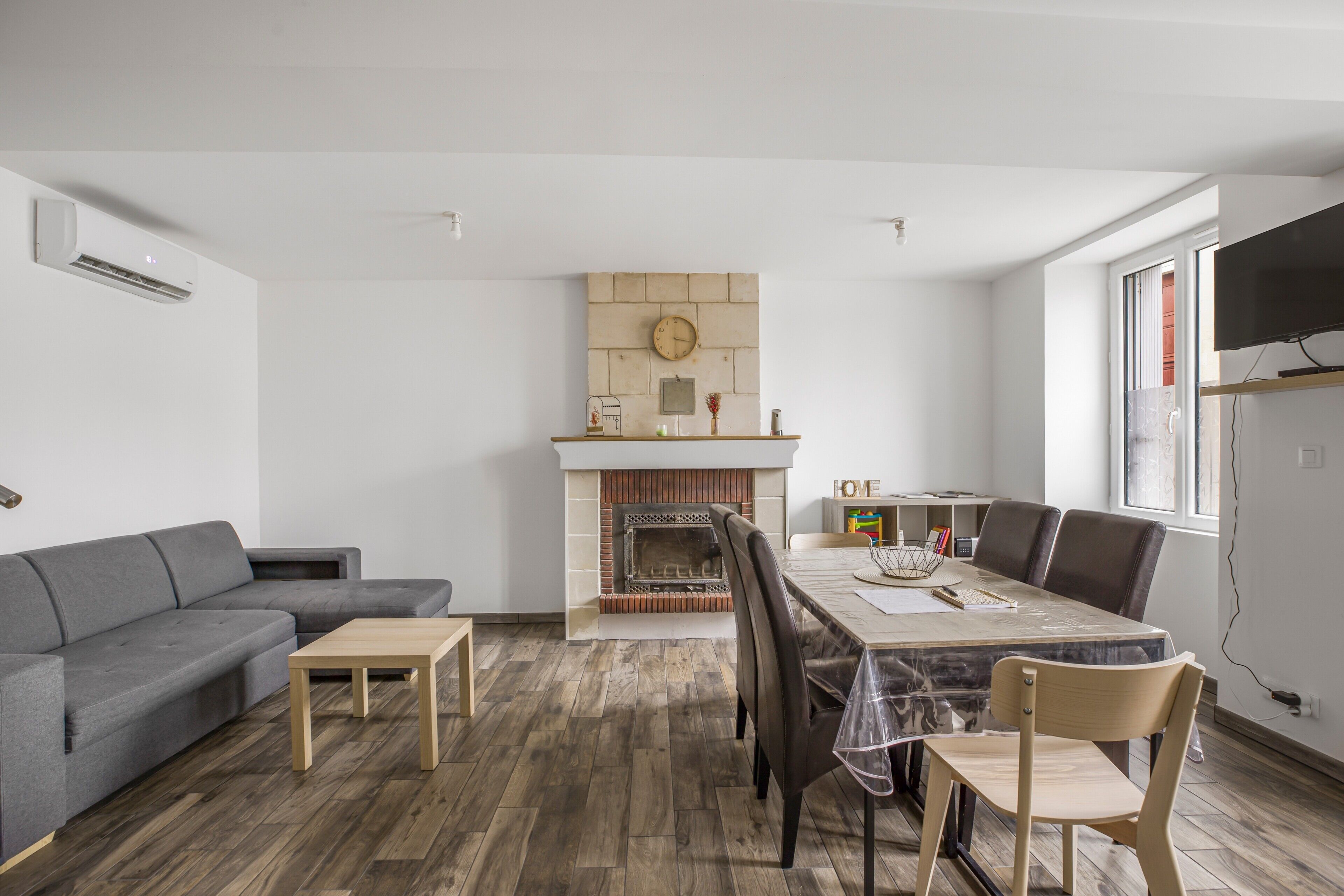 Een moderne woonkamer met een open haard, een eettafel met stoelen, een bank en een aan de muur bevestigde televisie.