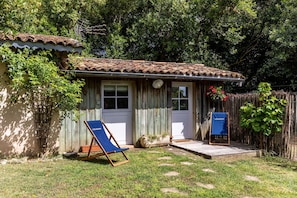 A small wooden house with a tiled roof, a front porch, and a garden area with a lawn and stepping stones.