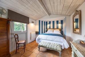 A bedroom with a bed, a chair, a bench, a window, and a mirror.