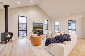A spacious living room with a fireplace, large windows, a sofa, and a coffee table. - Monthly Lease - Revival Retreat by Tahoe Getaways - 4BR in Downtown Truckee (Truckee)