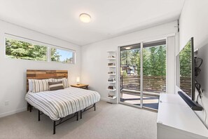 A bedroom with a bed, a bedside table, a bookshelf, a window, and a sliding glass door leading to an outdoor area. - Starfall Run at Palisades by Tahoe Getaways - Luxury 3BR, A/C & Bonus Room! (Alpine Meadows)
