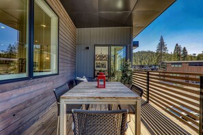 A wooden deck with a table and chairs, a red lantern, and a view of a forested area. - Starfall Run at Palisades by Tahoe Getaways - Luxury 3BR, A/C & Bonus Room! (Alpine Meadows)