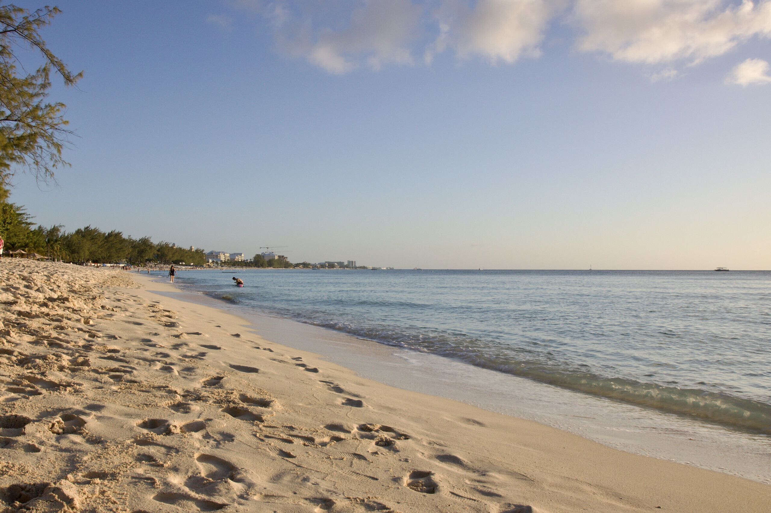 Une plage où l’on peut voir des empreintes de pas dans le sable, un ciel dégagé et une mer calme.