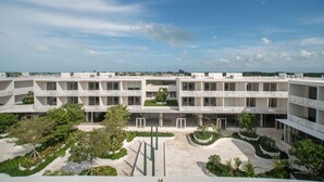 A modern multi-story building with a central courtyard, balconies, and surrounding greenery.