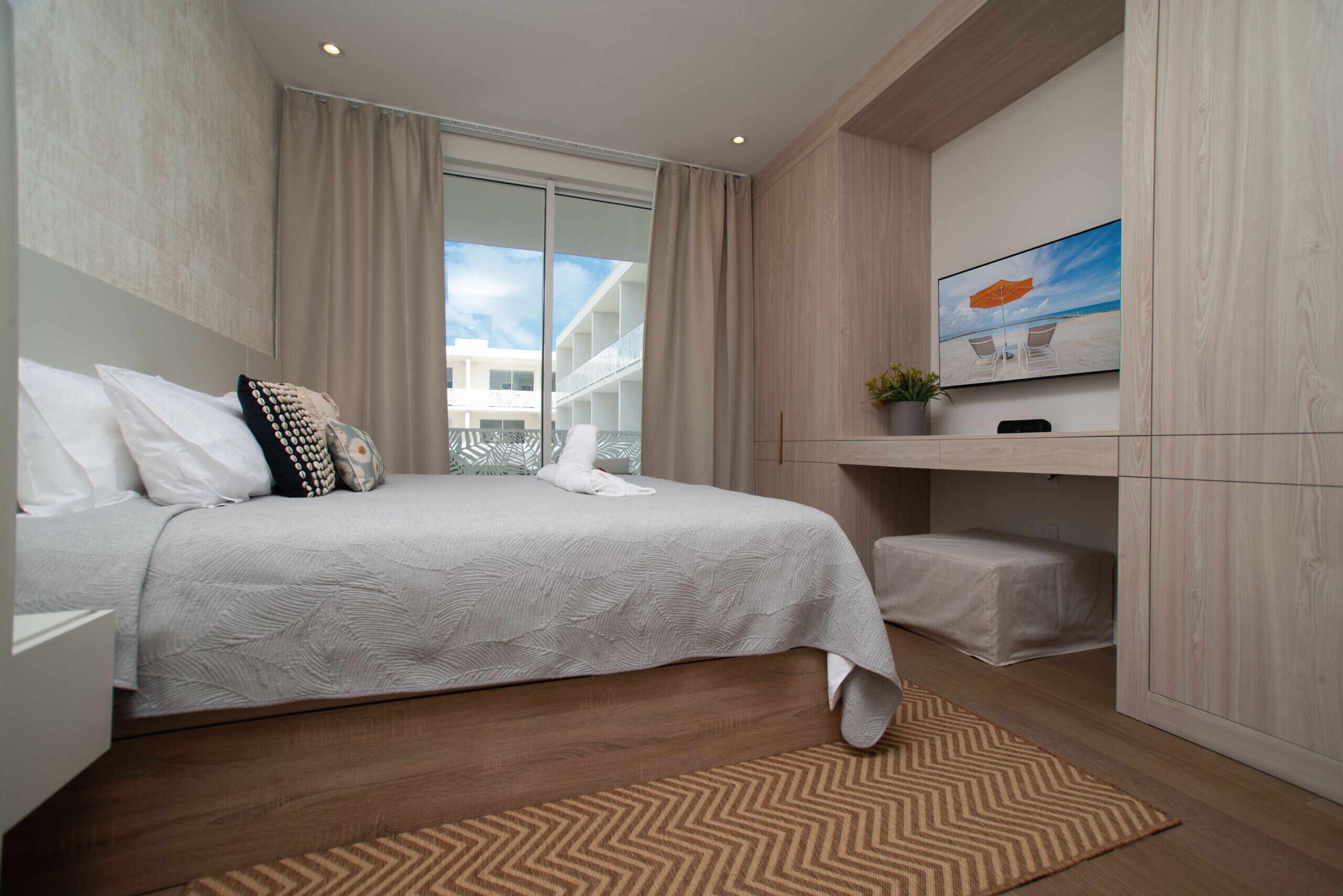 A modern hotel room with a large bed, a flat-screen TV, a small desk, and a window with a view of a building.