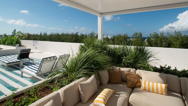 A covered outdoor seating area with a pool, lounge chairs, and a sofa with cushions.