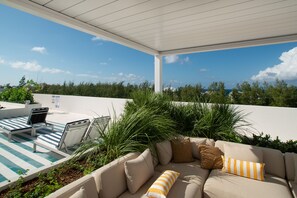 A covered outdoor seating area with a pool, lounge chairs, and a sofa with cushions. - Steps to Seven Mile Beach Luxe 2-Bed at Grove Too (Seven Mile Beach)