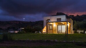 A modern house with a stone facade, large windows, and a well-lit interior. - Casa Maruzza | Scopello | Sea-view retreat with infinity pool (Castellammare del Golfo)