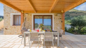 A covered outdoor dining area with a stone wall, a wooden ceiling, and a view of a hilly landscape. - Casa Maruzza | Scopello | Sea-view retreat with infinity pool (Castellammare del Golfo)