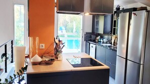 Et moderne køkken med en central ø, rustfrie stålensapparater og udsigt til en pool i baghaven.
