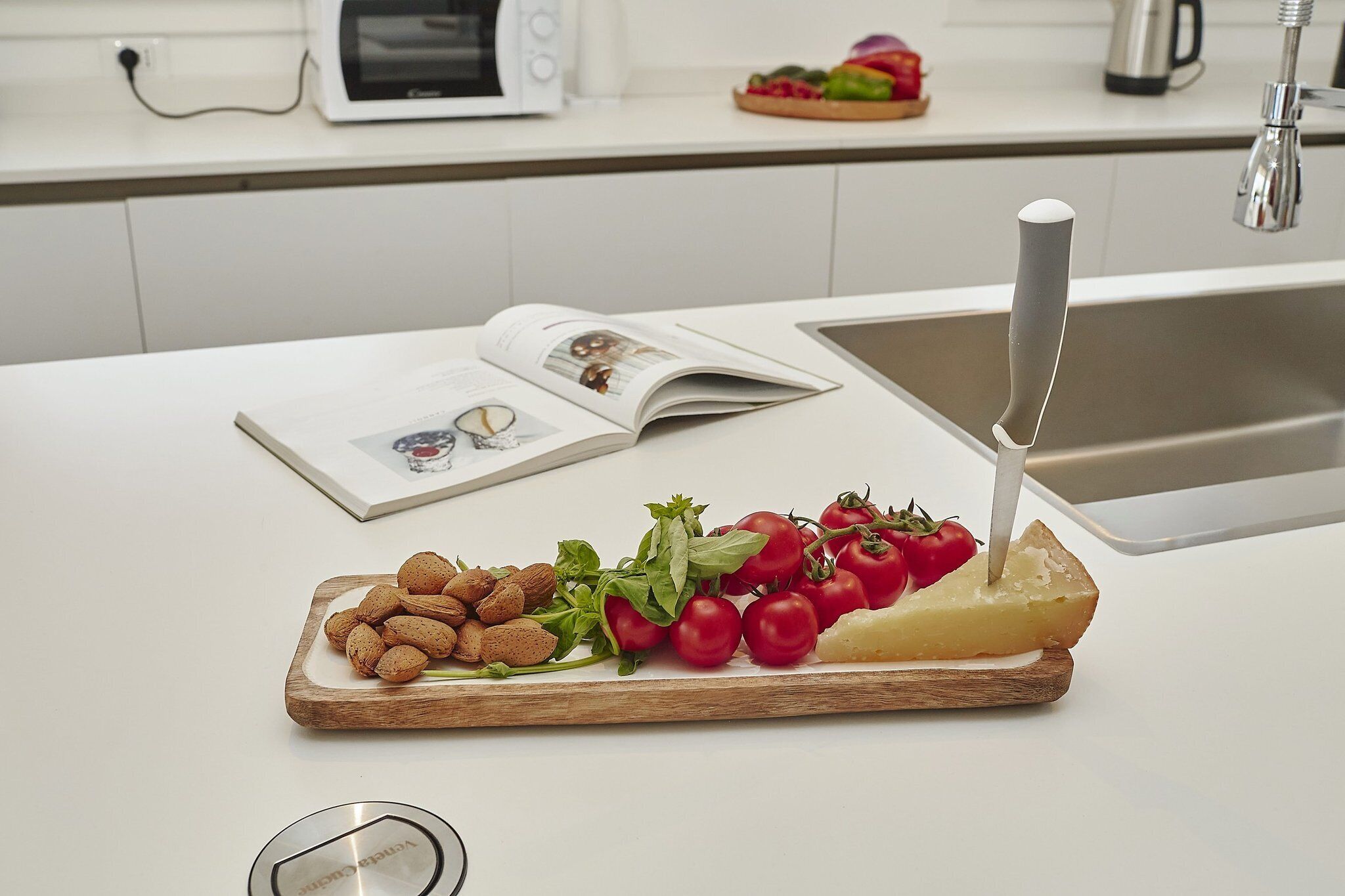 A kitchen counter with a cutting board holding almonds, tomatoes, and cheese.