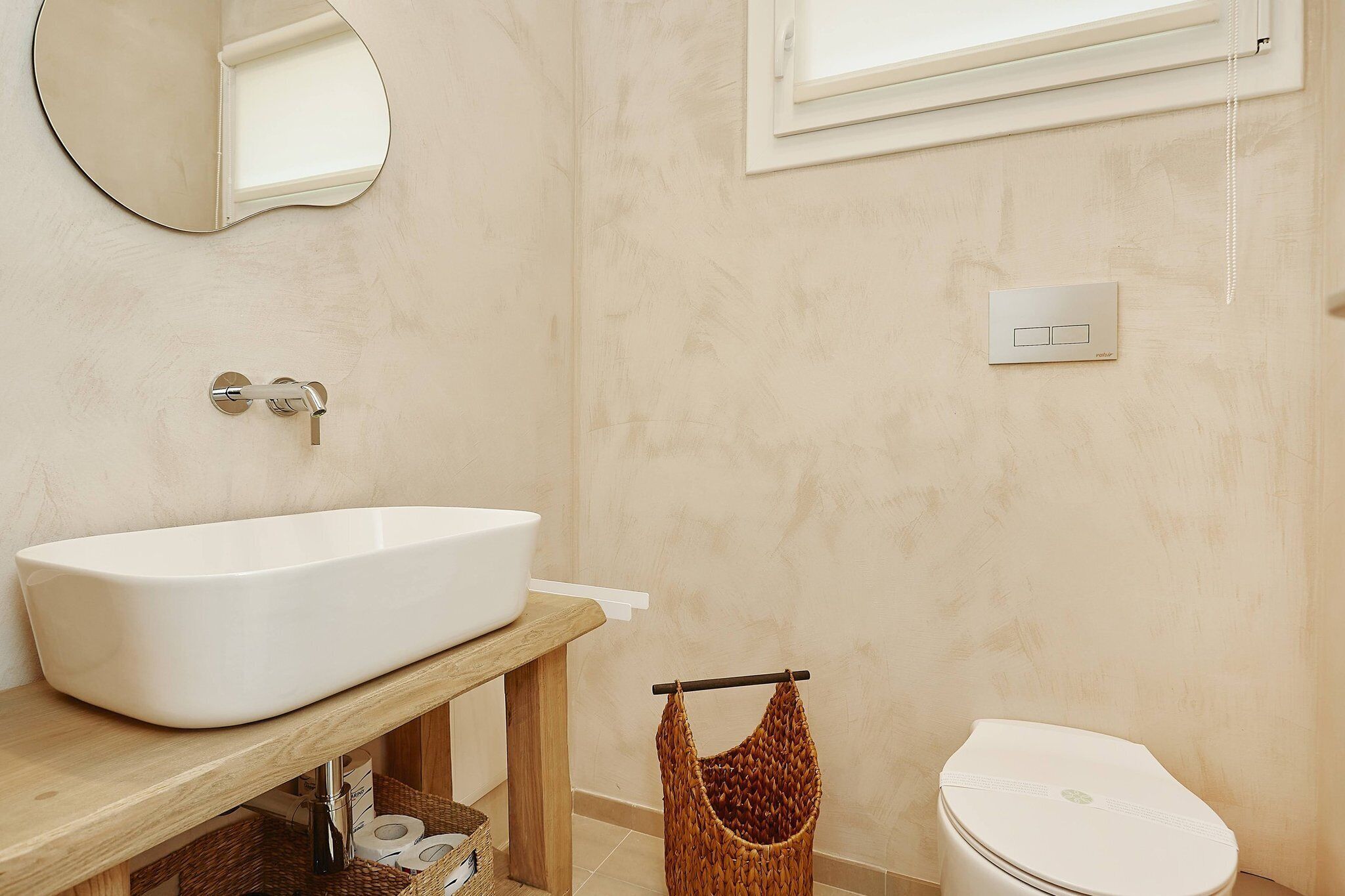 Ein Badezimmer mit freitstehender Badewanne, einem Holzwaschtisch, einer Toilette, einem hängenden Korbwannenaufsatz und einem wandmontierten Lichtschalter.