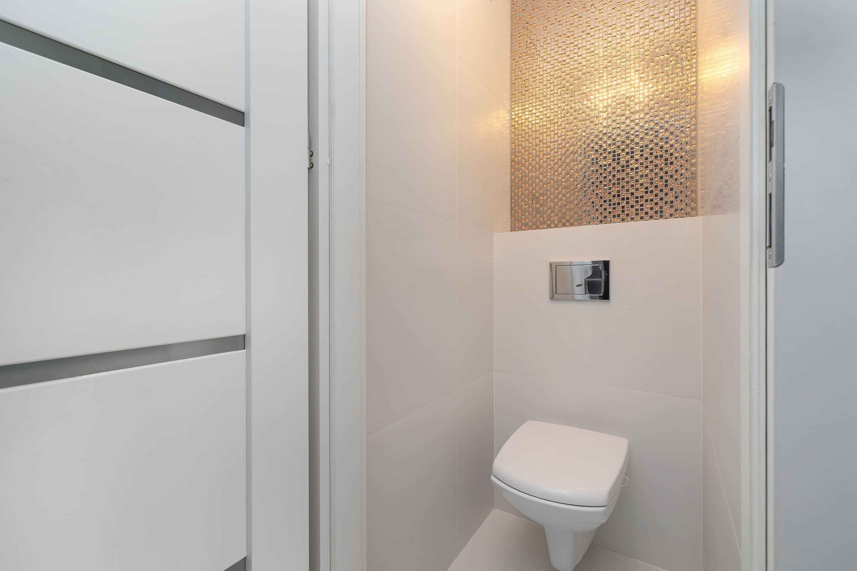 A modern bathroom with a white toilet, a wall-mounted bidet, and a textured decorative panel.
