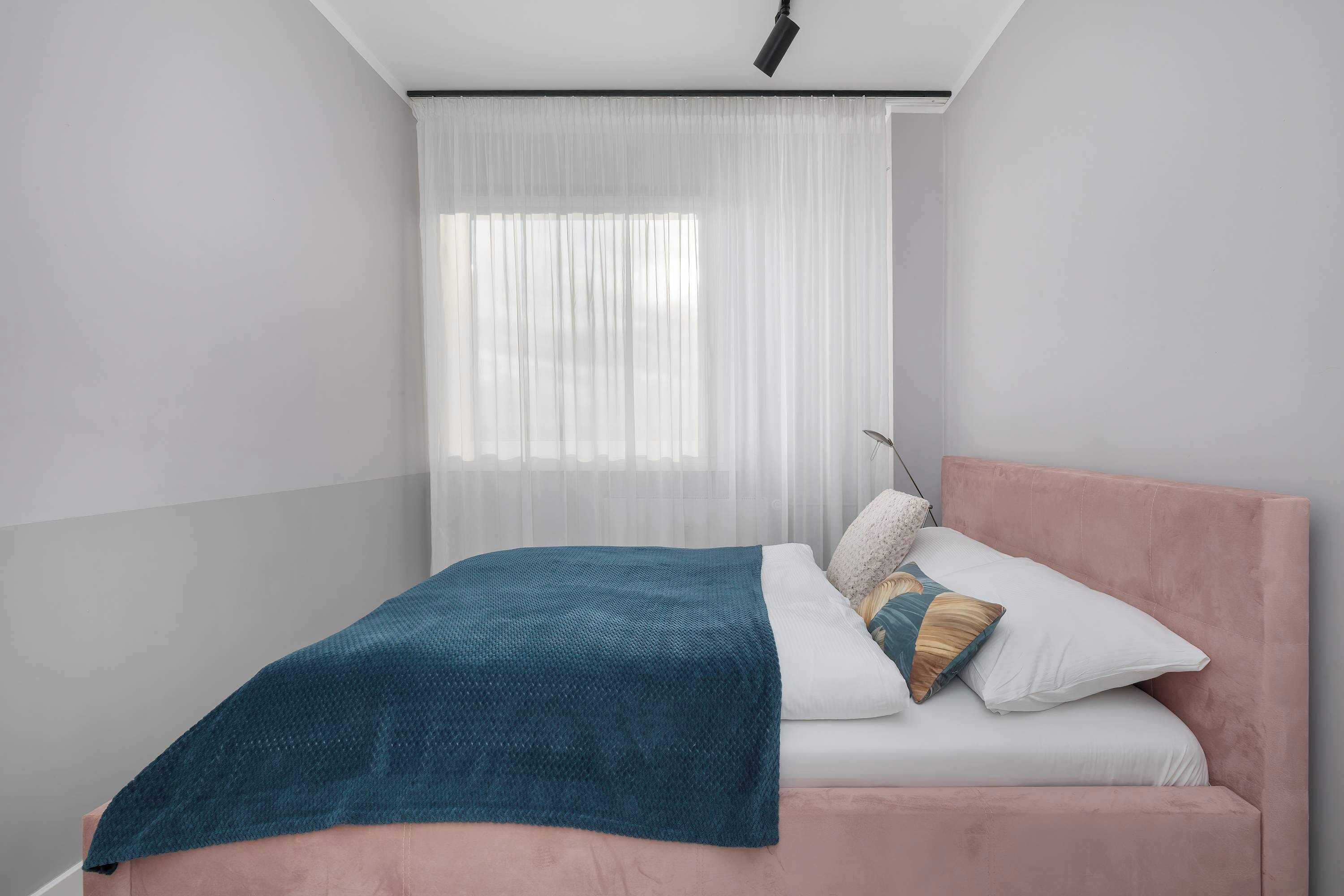 Une chambre à coucher avec un lit, des rideaux blancs et un luminaire au plafond.
