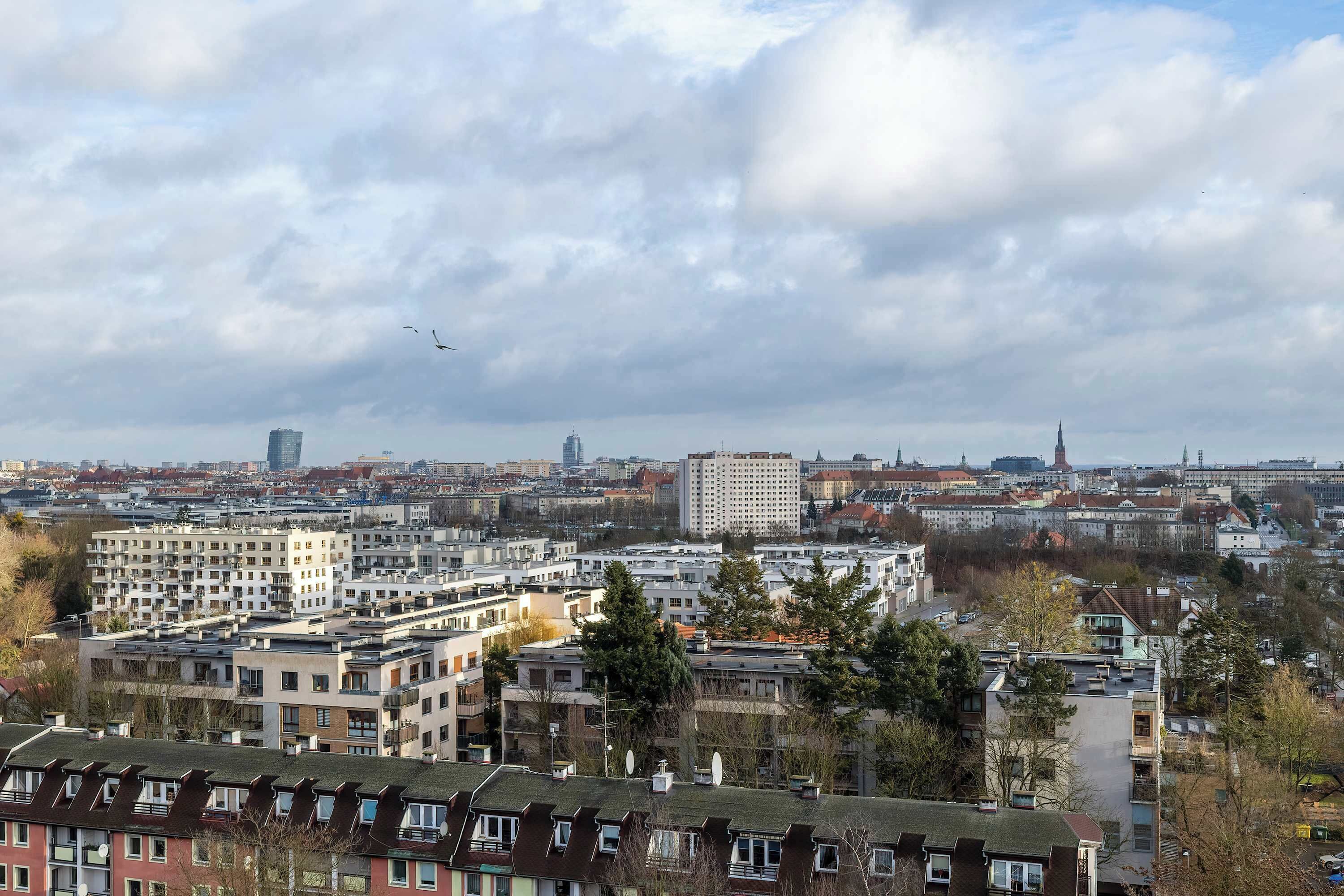 Une vue urbaine avec des bâtiments modernes, le clocher imposant d’une église et un oiseau volant dans le ciel.