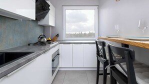 Una cocina compacta con armarios blancos, una encimera negra y una ventana con vistas a un área boscosa.