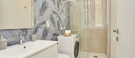 Une salle de bain moderne avec un lavabo, des toilettes et un lave-linge, le tout de couleur blanche.