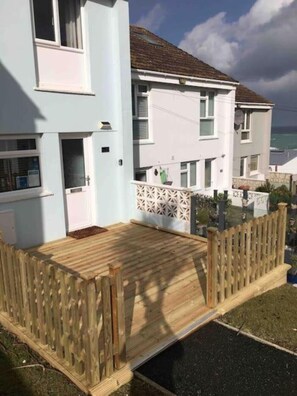 Ein zweistöckiges Wohnhaus mit Flachdach, einer Holzdachterrasse und einem weißen Zaun.