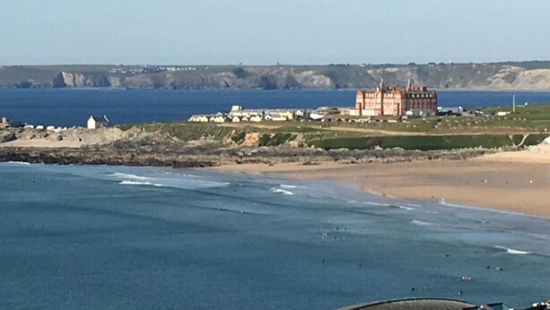 Ein Küstenblick mit einem markanten Gebäude, einem Strand und Klippen im Hintergrund.