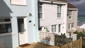 Ein zweigeschossiges Wohngebäude mit hellblauer Fassade, einer Holzterrasse und einem dekorativen Zaun.