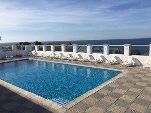 Ein Schwimmbecken mit weißen Liegestühlen und Blick aufs Meer.