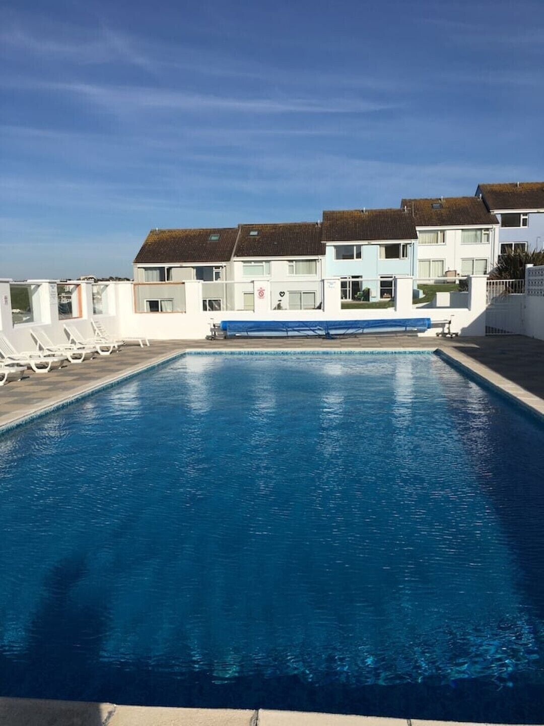 En swimmingpool med solstolar och en rad byggnader i bakgrunden.