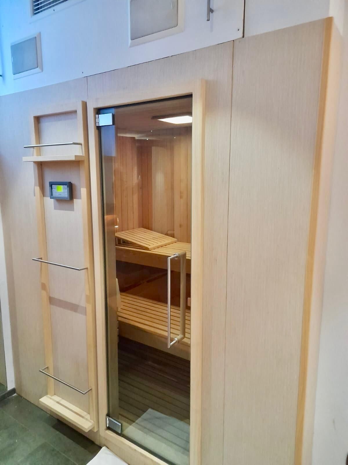 A wooden sauna with a glass door, shelves, and a control panel.