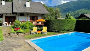 Et hus med swimmingpool, omgivet af en have med stole og en hæk.
