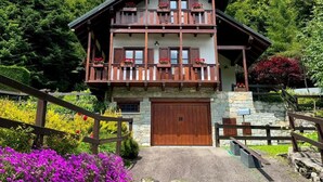 En toetages chalet med stenvæg, gelændinger af træ og en garageport i træ.