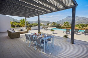 A covered outdoor dining area with a pool, seating, and a view of mountains. - Casa Fior di Mandorla | Castellammare del Golfo | Sea View | Infinity Pool (Castellammare del Golfo)