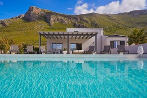 Eine moderne Villa mit Pool, Sitzgelegenheiten im Freien und Bergblick.