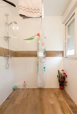 A bathroom with a shower, a towel hanging on the wall, a window, and a potted plant. - Suite Escale Ground Floor (Plouédern)