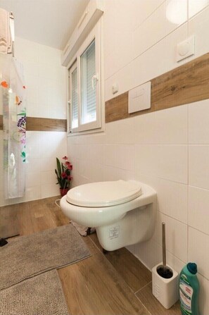 Une salle de bain avec des toilettes, une fenêtre, une plante en pot et une brosse de nettoyage.