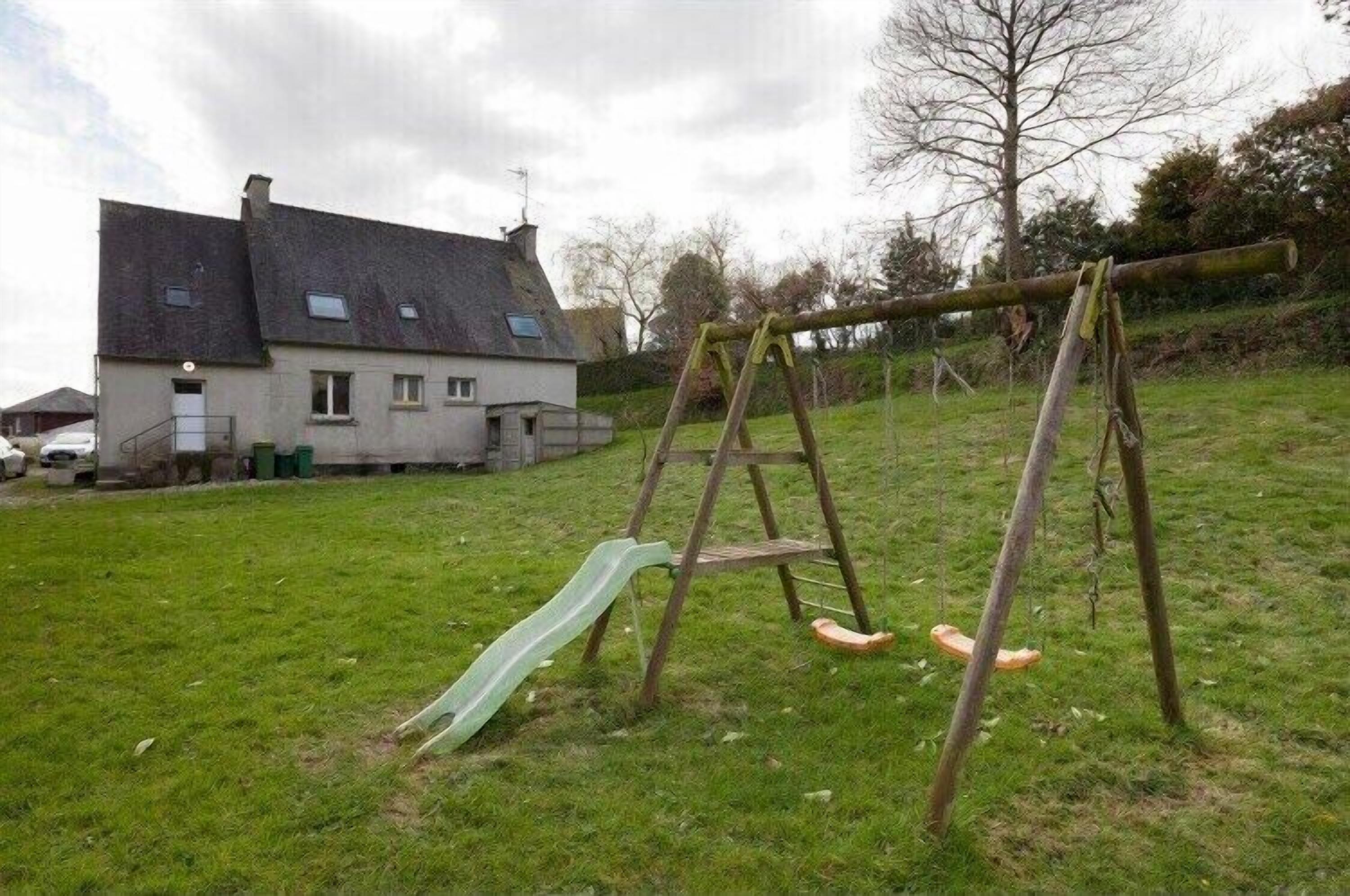 Un ensemble de jeux d’extérieur en bois, avec un toboggan vert, installé sur une pelouse, avec une maison en arrière-plan.
