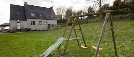 Un ensemble de jeux d’extérieur en bois, avec un toboggan vert, installé sur une pelouse, avec une maison en arrière-plan.