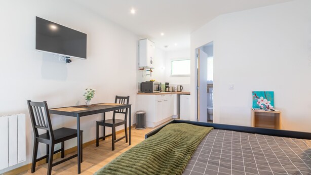 A modern room with a bed, a desk, and a chair. There is a TV mounted on the wall, a window, and a painting on the wall. - New Studio Rivage Garden Floor (Plouédern)
