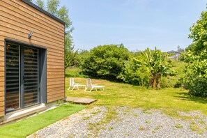 A modern building with a wooden exterior, a gravel driveway, and a grassy area with two white chairs.